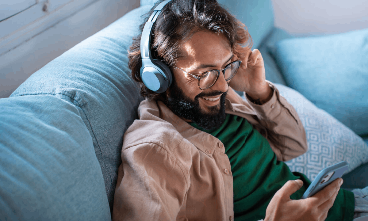 Popular Funeral Songs and Their Significance A man wearing headphones and smiling while listening to music on his phone as he relaxes on a couch.